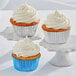 Three Enjay white foil cupcakes with white frosting on a white pedestal.