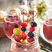 A glass of fruit on stainless steel skewers in a glass of fruit juice.