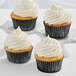 Three Enjay black foil baking cups with cupcakes with white frosting.