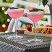 Two Acopa Endure Tritan plastic coupe glasses filled with pink drinks on a table.