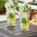 Two Acopa Tritan plastic highball glasses with lemonade, limes, and mint leaves on a table.