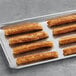 A tray of White Toque fried churros on a gray surface.