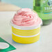 A yellow paper cup of pink frozen yogurt with a spoon in it and a dome lid on top.