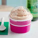 A Choice pink paper frozen yogurt cup with dome lid and a plastic spoon on top of a cup of frozen yogurt.