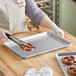 A person wearing gloves holds a pretzel over a Nordic Ware aluminum sheet pan.