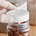 A person's hand holding a jar of spices with a white unlined polypropylene spice cap.