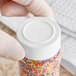 A person holding a jar of colorful sprinkles with a white cap.