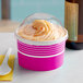 A pink Choice paper cup filled with frozen yogurt and topped with a dome lid and spoon on a counter.
