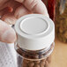A person holding a white jar with a white 48/485 unlined polypropylene spice cap on it.