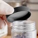 A hand holding a clear plastic container with a black 53/400 polypropylene cap filled with lavender.