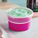 A pink paper food cup with a flat lid containing green frozen yogurt.