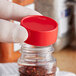 A person holding a plastic container with a red 43/485 unlined polypropylene spice cap on it.