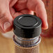 A person holding a jar with a black unlined polypropylene spice cap on it.