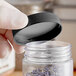 A hand holding a clear plastic container of lavender with a black polypropylene cap.