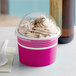 A pink Choice paper frozen yogurt cup with a dome lid filled with ice cream on a counter.