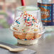 A clear plastic dessert cup with whipped cream and sprinkles on top in a plastic container.