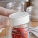 A person holding a white plastic jar of dried red peppers.