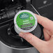 A hand holding a Green Mountain Coffee Roasters Dark Magic K-Cup Pod with a green and white circle on the counter.
