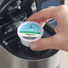 A hand placing a Caribou Coffee Decaf K-Cup pod in a coffee maker.