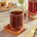 A glass mug of Caribou Coffee Mahogany Blend on a wooden coaster.