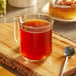 A glass mug of Cinnabon Classic Cinnamon Roll coffee on a wooden board with a spoon.