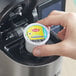 A hand holds a small white plastic container of Lipton Unsweetened Iced Tea K-Cup Pods.