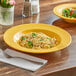 A yellow Acopa Foundations melamine pasta bowl with pasta and broccoli on a table.