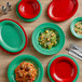 A wood table set with Acopa Foundations green melamine dinnerware, including a green plate with a salad, and red and green bowls.