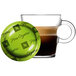 A glass cup of Nespresso Professional Peru Organic coffee next to a coffee pod on a green saucer.