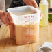A person pouring brown liquid from a measuring cup into a Cambro FreshPro food storage container.