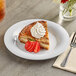 A slice of pie with whipped cream and strawberries on an Acopa Foundations white melamine plate.