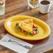 A yellow Acopa Foundations melamine platter with a slice of food on it.