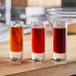 A group of shot glasses with different colored liquid on a table.
