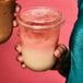 Two people holding Tossware plastic cups with pink and white liquid.
