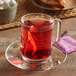 A glass mug of Harney & Sons Raspberry Herbal Tea with a tea bag on a saucer.