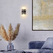 A Globe Glam Matte Black wall sconce with ribbed glass in a white room over a blue couch with a white pillow.