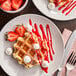 A plate of Eastern Standard Provisions Plain Belgian Liege Waffles with strawberries and whipped cream with a fork and knife.