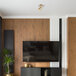 A Globe Pratt modern matte brass track light in a lounge area with wooden paneling and a TV on the wall.