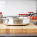 A Vollrath Wear-Ever saute pan with a tomato on a wooden cutting board.
