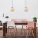 A restaurant dining area with a wooden table and pink chairs under a Novogratz matte brass pendant light.
