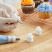 A hand using a Wilton plastic coupler on a pastry bag to pipe yellow frosting on a cupcake.