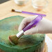 A gloved hand using a Wilton decorating brush to paint a cake.