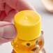 A hand holding a small plastic bottle of honey with a yellow ribbed cap.