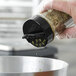 A hand using a black dual flapper spice lid to sprinkle herbs.