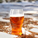 A Tossware plastic pint glass of beer with foam on the snow.