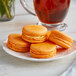 A white plate of Coco Bakery mango passionfruit macarons with orange shells.