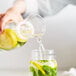 A person pouring water from a Tossware plastic carafe into a glass with lemon and mint.