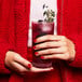 A woman in a red jacket holding a Tossware Reserve highball glass with a drink and garnish.