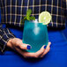 A woman holding a Tossware Reserve Go-To stemless wine glass with a blue drink and a lime.