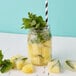 A Tossware plastic Mason jar filled with ice, mint, and pineapple with a straw.